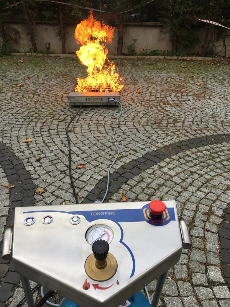 TOKO FIRE yangın eğitim simülatörü: ön planda kontrol paneli, arkada gaz beslemeli tavada gerçek alev